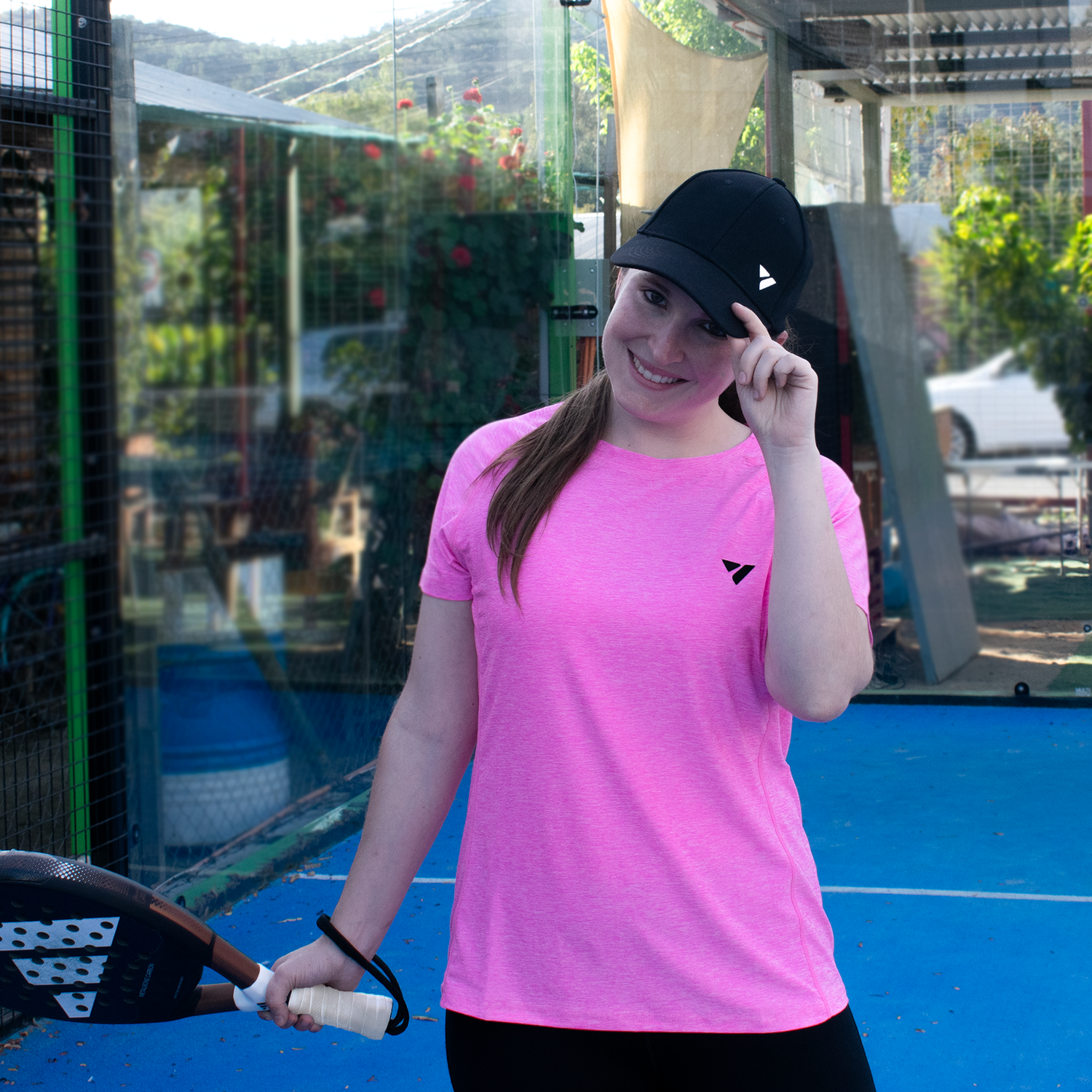 mujer en cancha de pádel con pala en la mano y sosteniendo gorra en su cabeza