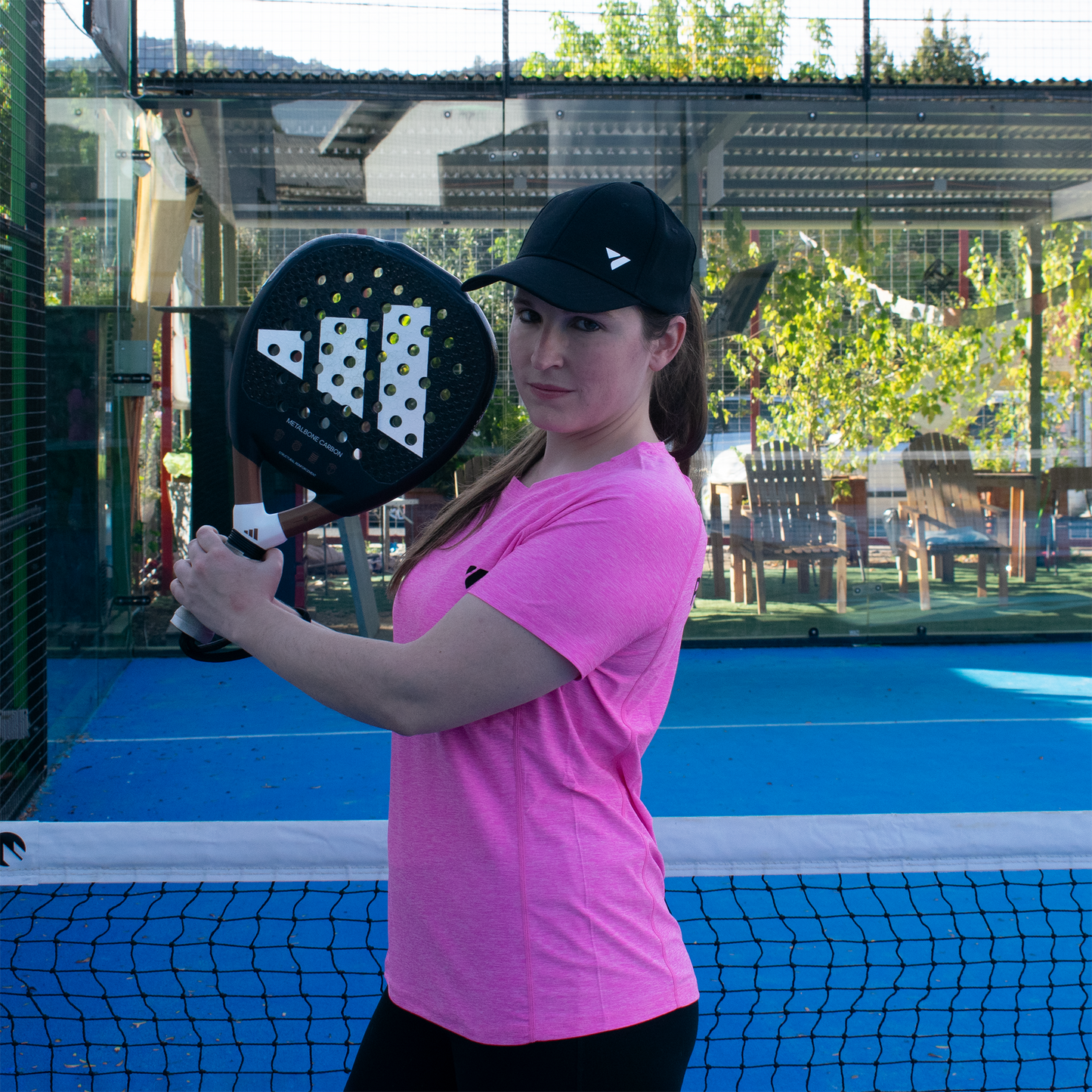 mujer de lado frente a la red en cancha de pádel sosteniendo su pala con ambas manos