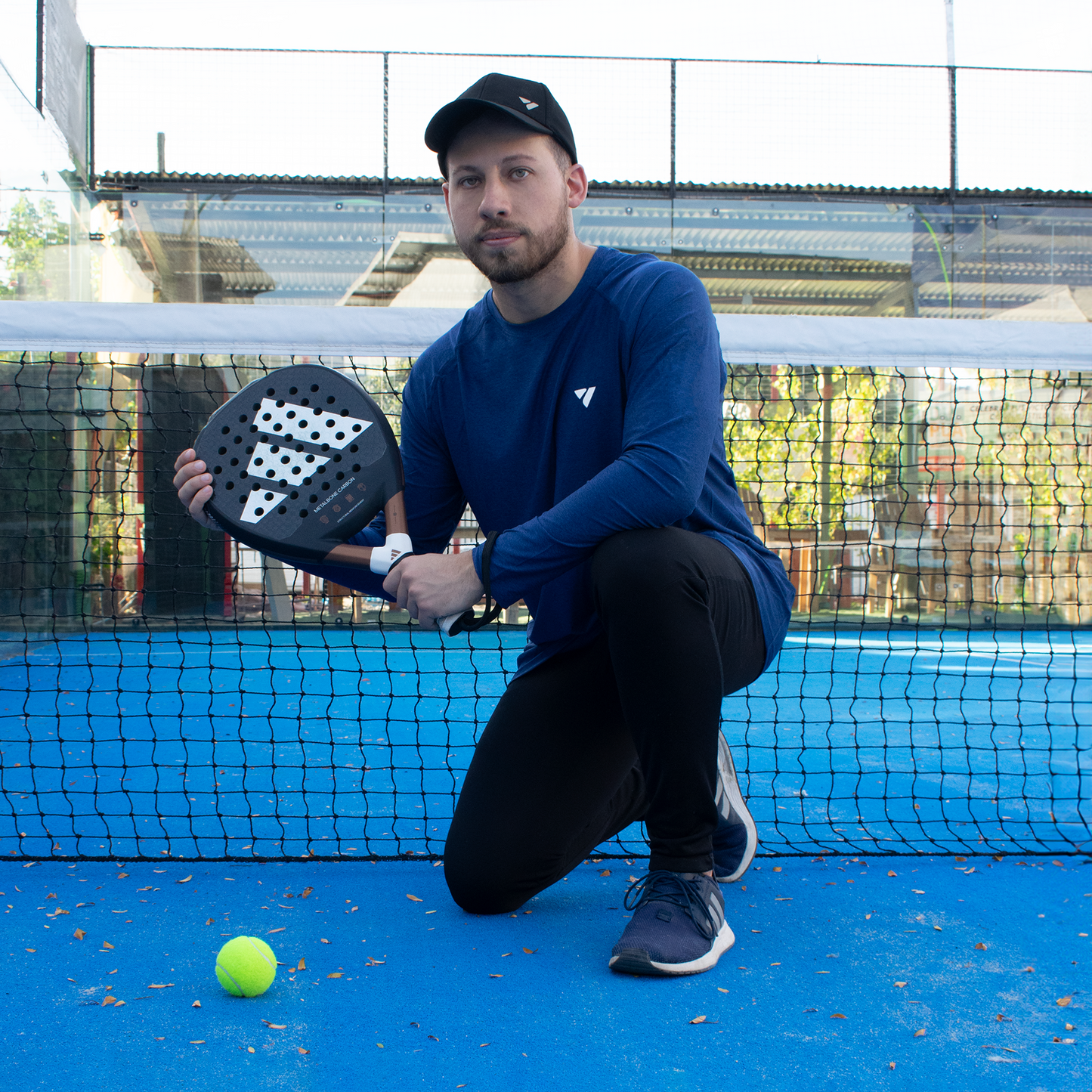 hombre arrodillado en cancha de pádel, sosteniendo su pala con pelota en el suelo