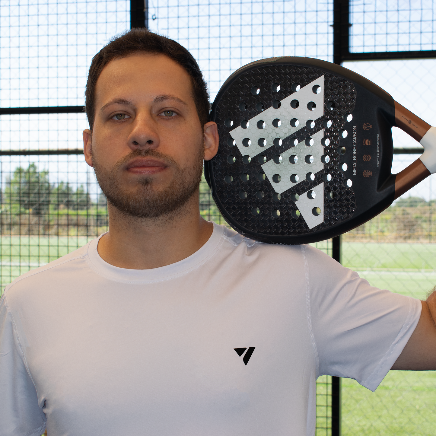 modelo usando polera blanca con logo negro en el pecho en cancha de pádel con pala en la cabeza