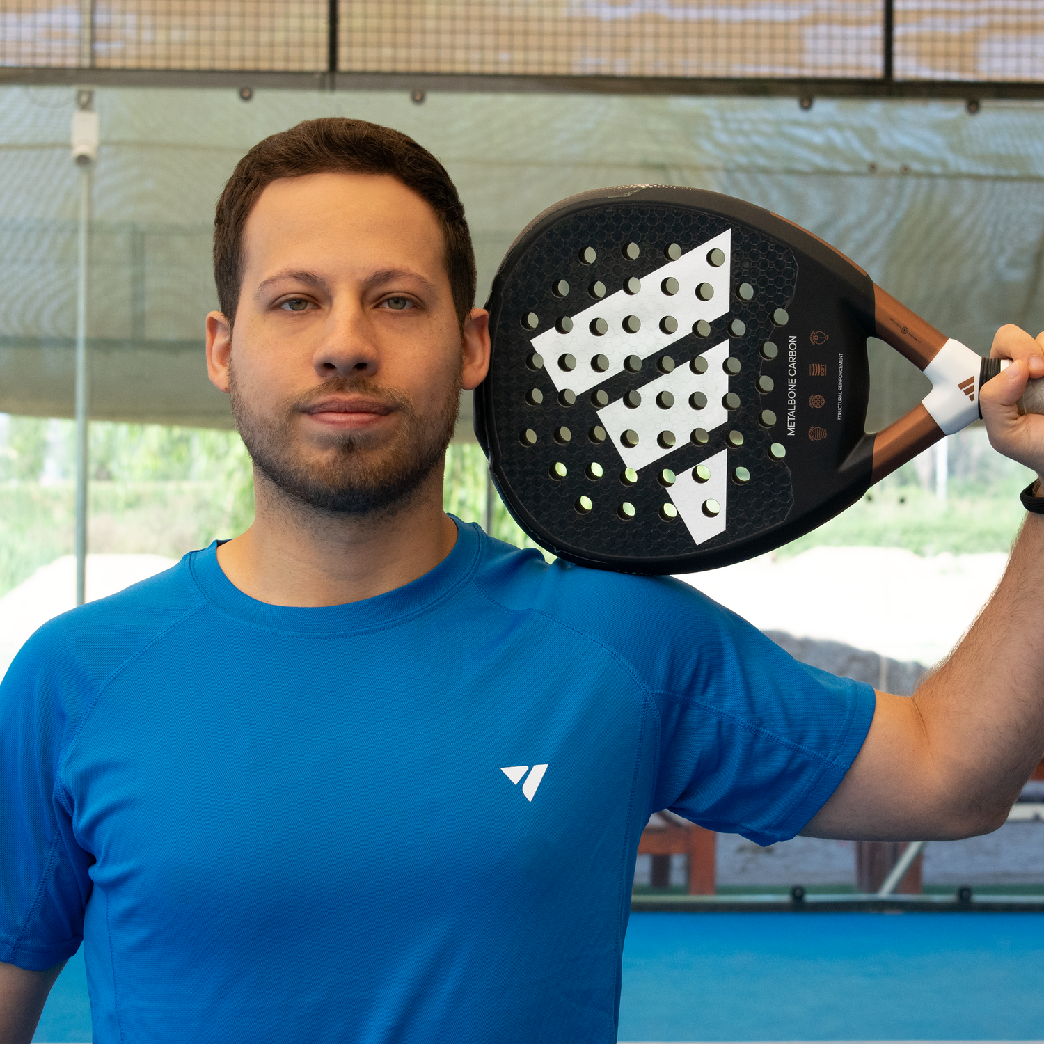 hombre sosteniendo pala de pádel sobre su hombro en cancha de padel